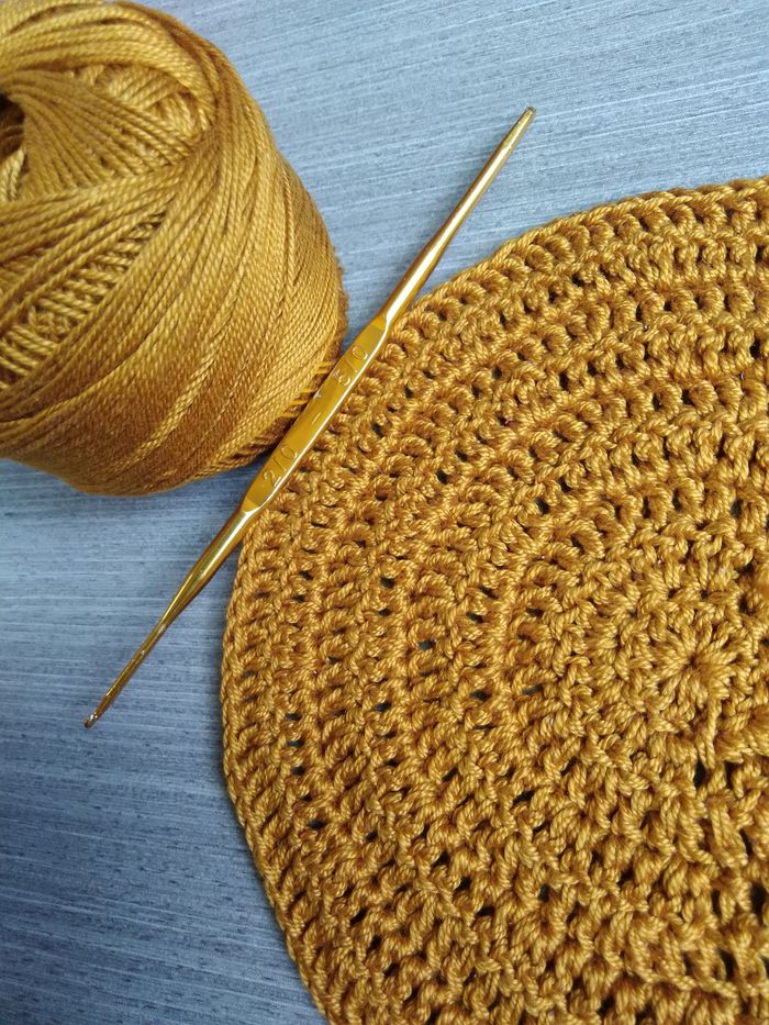 Close-up of golden yarn and crochet hook on a textured surface.